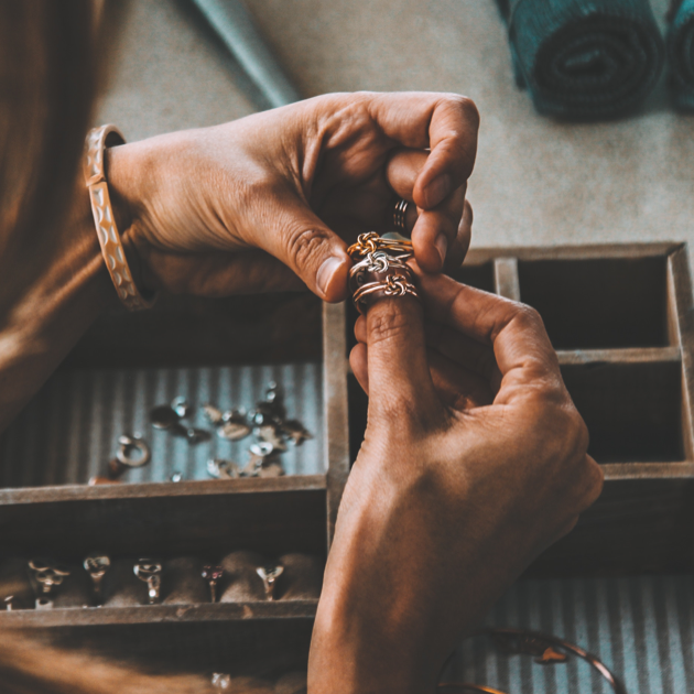 One of our jewel crafters holding 3 knot rings - a gold, a silver, and a rose gold.